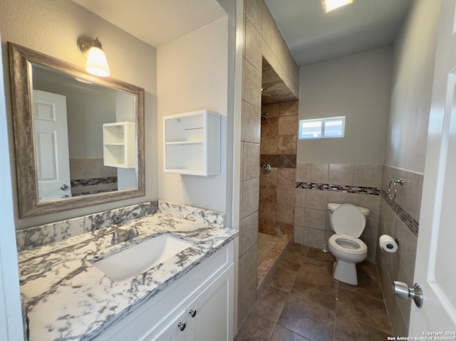 bathroom with a tile shower, tile patterned floors, toilet, vanity, and tile walls