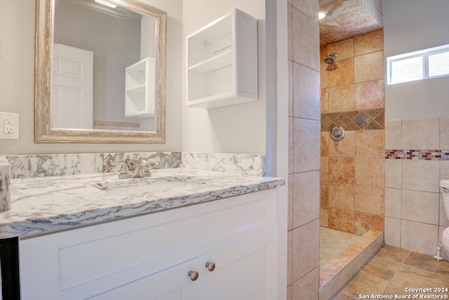 bathroom with tile patterned flooring, vanity, toilet, and a tile shower