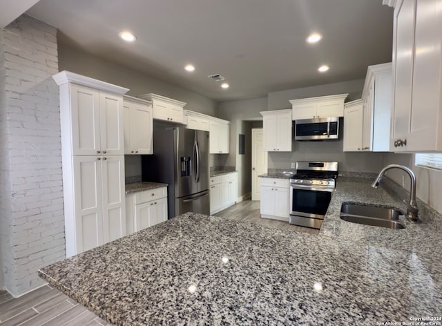 kitchen with appliances with stainless steel finishes, light wood-type flooring, sink, dark stone countertops, and white cabinets