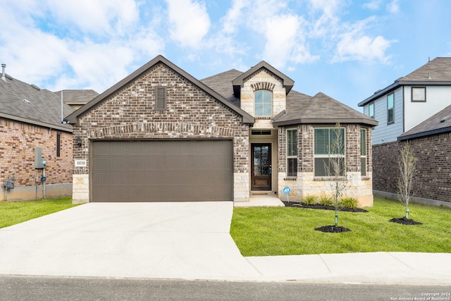 french country inspired facade with a front lawn, concrete driveway, brick siding, and an attached garage