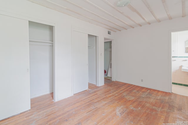 unfurnished bedroom with light hardwood / wood-style flooring, connected bathroom, and two closets