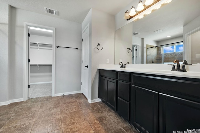 full bath with visible vents, baseboards, a sink, a tile shower, and a walk in closet