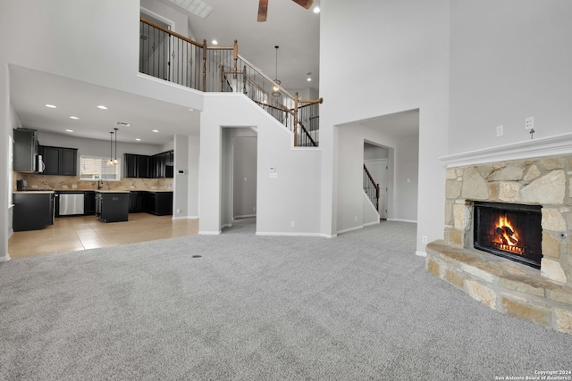 unfurnished living room with a high ceiling, light colored carpet, sink, and a stone fireplace