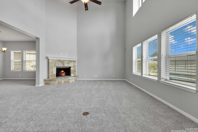 unfurnished living room featuring a high ceiling, carpet, ceiling fan, and a stone fireplace