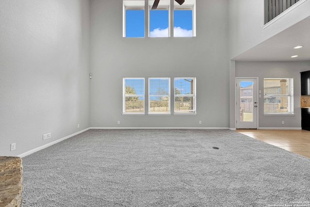 unfurnished living room with a high ceiling, light carpet, and ceiling fan