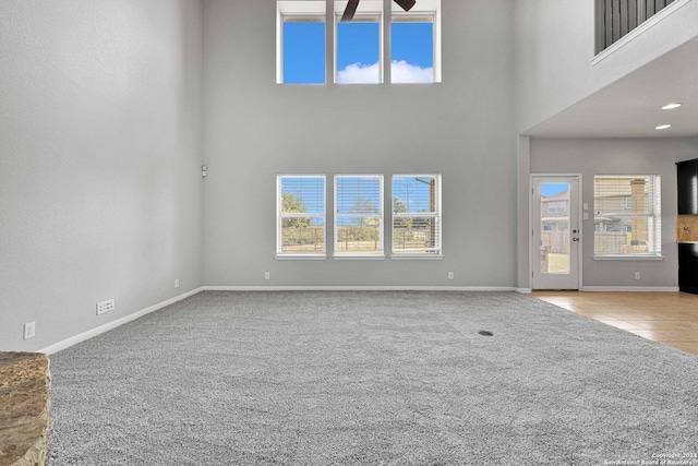 unfurnished living room featuring a high ceiling, baseboards, a ceiling fan, and carpet floors