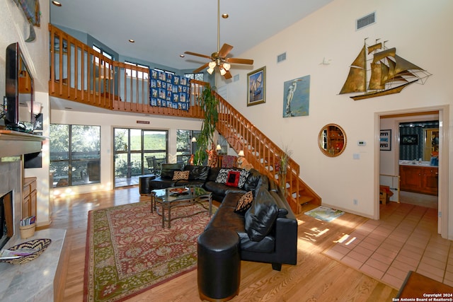 living room with a fireplace, a high ceiling, light hardwood / wood-style flooring, and ceiling fan