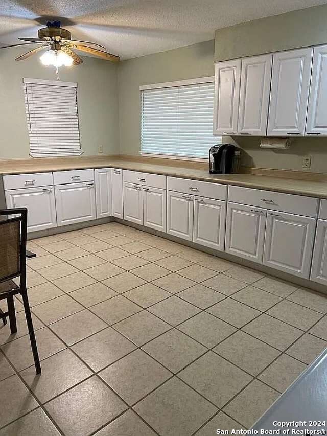 kitchen featuring a textured ceiling, ceiling fan, light tile patterned floors, and white cabinets