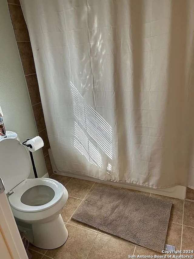 bathroom with toilet, a shower with shower curtain, and tile patterned floors