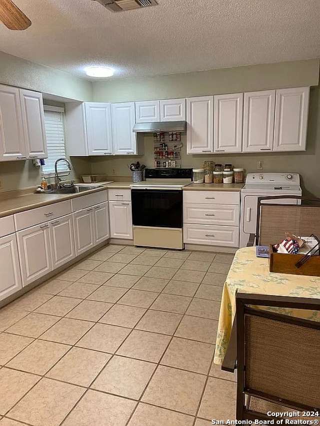 kitchen with washer / dryer, a textured ceiling, white cabinets, light tile patterned floors, and white range with electric cooktop