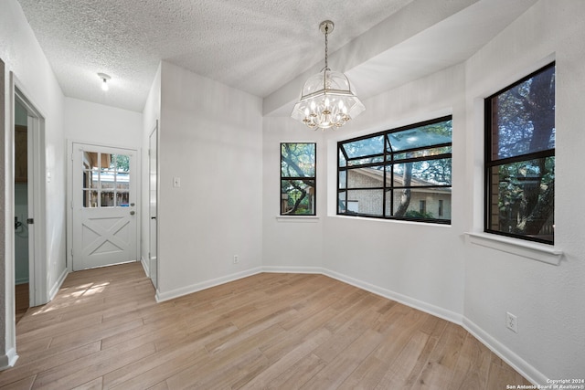 unfurnished dining area with an inviting chandelier, light hardwood / wood-style floors, plenty of natural light, and a textured ceiling