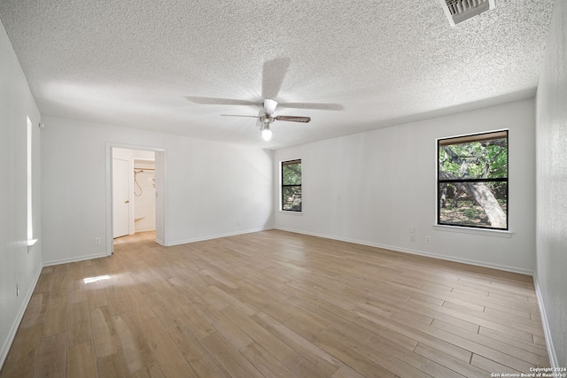 empty room with a textured ceiling, light wood-type flooring, and a healthy amount of sunlight