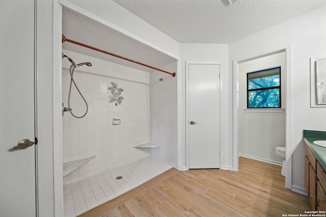 bathroom with vanity, a textured ceiling, a tile shower, toilet, and hardwood / wood-style floors