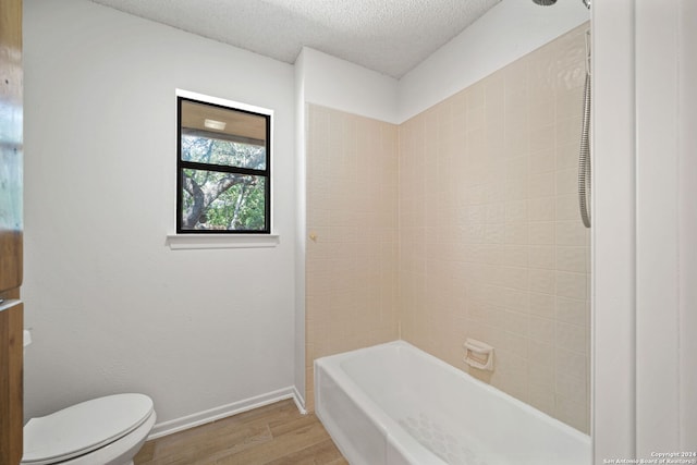 bathroom with a textured ceiling, hardwood / wood-style floors, toilet, and tiled shower / bath