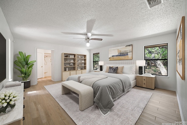 bedroom featuring ceiling fan, a textured ceiling, light hardwood / wood-style flooring, and connected bathroom