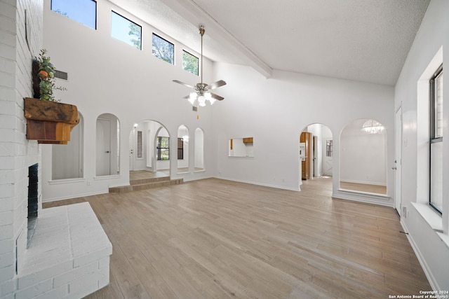 unfurnished living room with a textured ceiling, a fireplace, light hardwood / wood-style flooring, and high vaulted ceiling