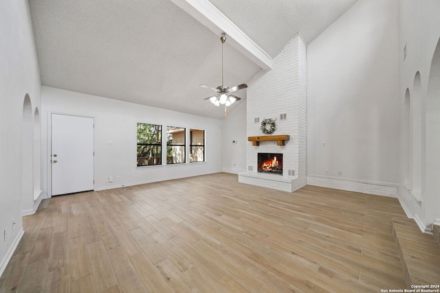 unfurnished living room featuring light hardwood / wood-style floors, a textured ceiling, a fireplace, high vaulted ceiling, and ceiling fan