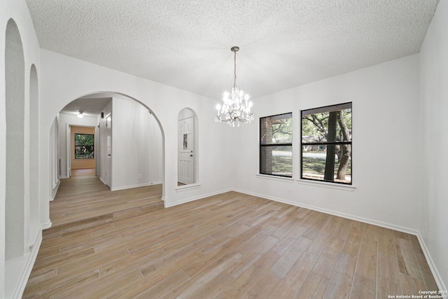 unfurnished room with light wood-type flooring, a chandelier, and a textured ceiling