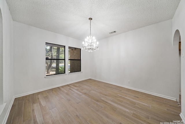 spare room featuring a notable chandelier, light wood-type flooring, and a textured ceiling