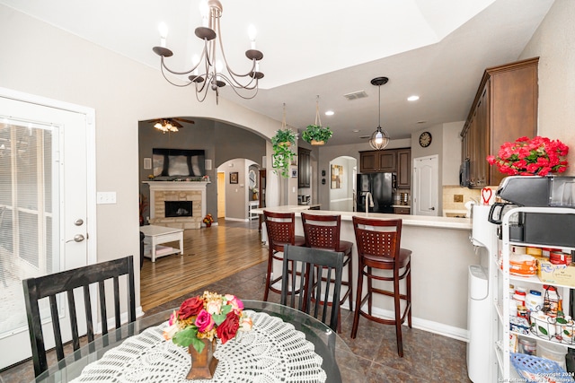 dining area with ceiling fan with notable chandelier, dark hardwood / wood-style floors, and a stone fireplace