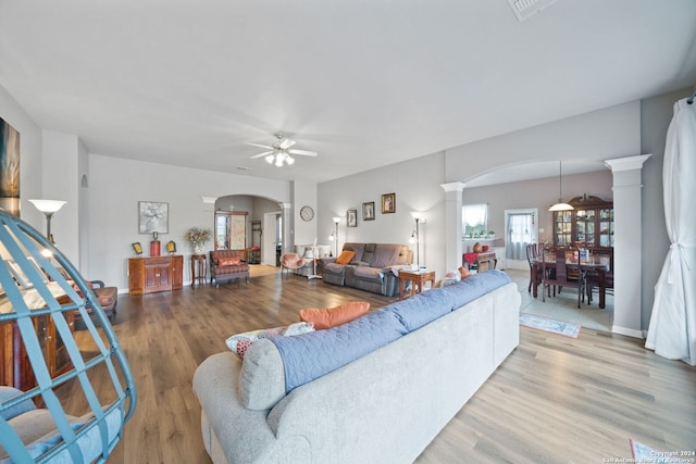 living room with light hardwood / wood-style flooring, ceiling fan, and ornate columns