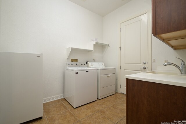 clothes washing area featuring separate washer and dryer, sink, light tile patterned floors, and cabinets