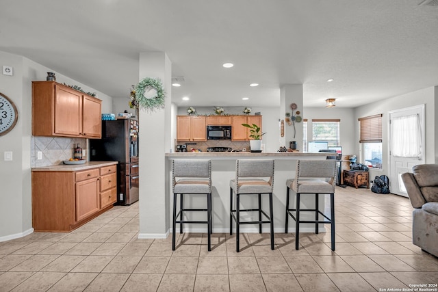 kitchen featuring stainless steel refrigerator with ice dispenser, backsplash, a kitchen bar, and light tile patterned flooring