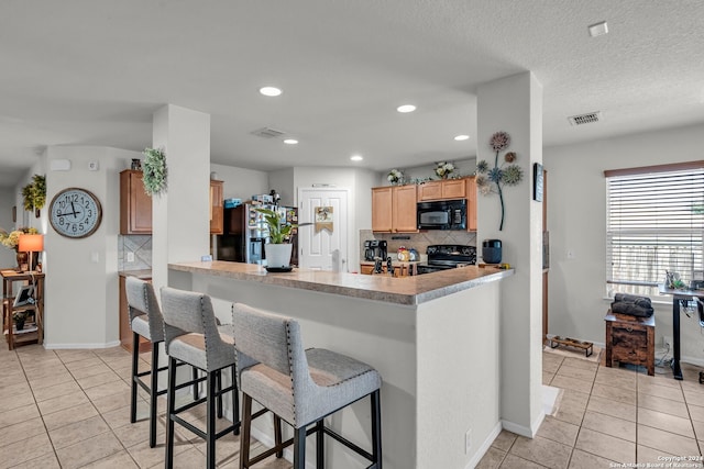 kitchen with a breakfast bar, tasteful backsplash, kitchen peninsula, light tile patterned floors, and black appliances