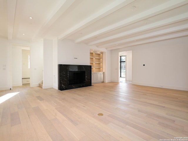 unfurnished living room with beamed ceiling, built in features, a premium fireplace, and light wood-type flooring