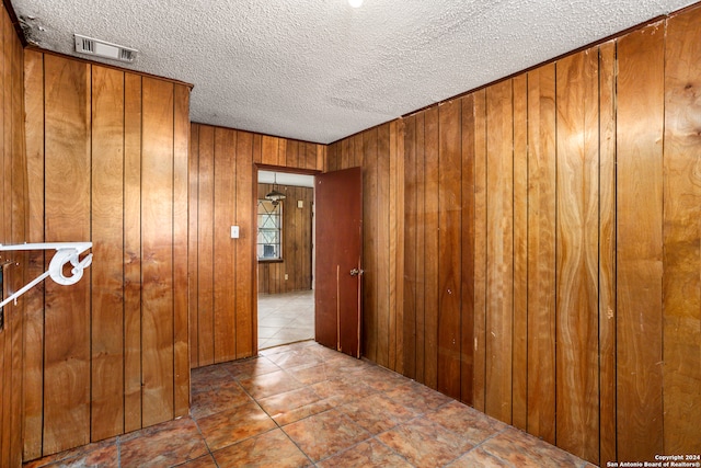 hall featuring tile patterned flooring, wooden walls, and a textured ceiling