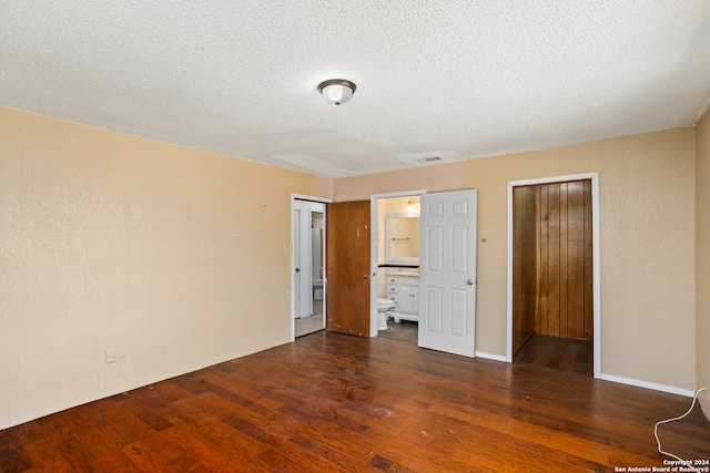 unfurnished bedroom featuring a textured ceiling, dark hardwood / wood-style floors, and ensuite bathroom