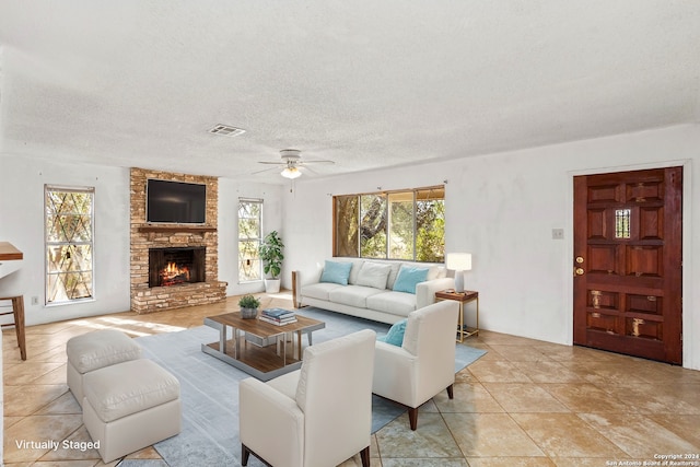 living room with ceiling fan, a stone fireplace, light tile patterned floors, and a textured ceiling