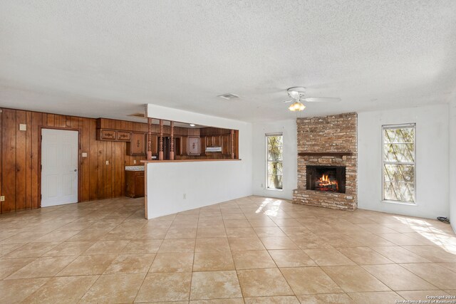 unfurnished living room featuring wood walls, ceiling fan, a fireplace, light tile patterned floors, and a textured ceiling