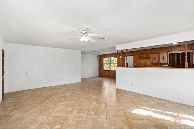 tiled spare room featuring a textured ceiling, wooden walls, and ceiling fan