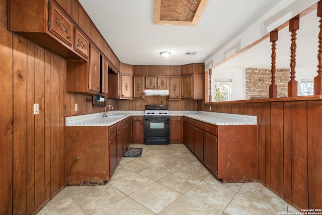 kitchen with gas range gas stove, sink, wood walls, light tile patterned floors, and a textured ceiling