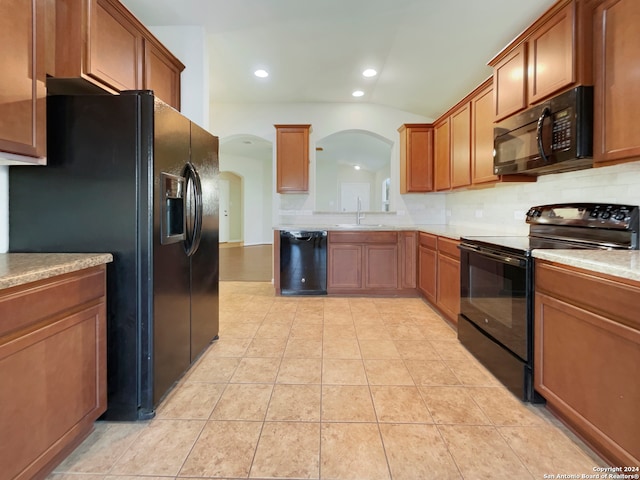 kitchen featuring lofted ceiling, light tile patterned floors, sink, tasteful backsplash, and black appliances