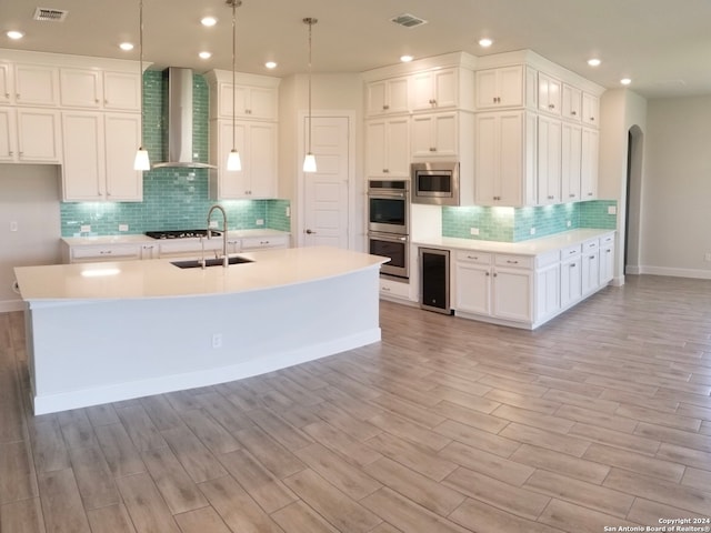 kitchen featuring wall chimney range hood, a kitchen island with sink, decorative light fixtures, sink, and stainless steel appliances