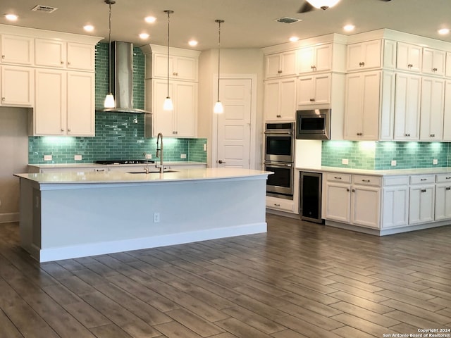 kitchen featuring white cabinets, wall chimney range hood, appliances with stainless steel finishes, decorative light fixtures, and backsplash