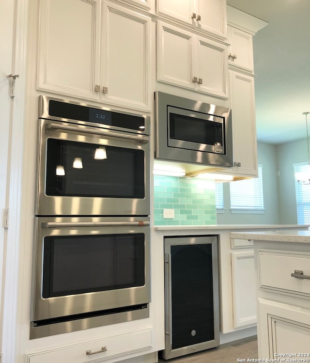 kitchen featuring wine cooler, stainless steel appliances, white cabinetry, and decorative backsplash