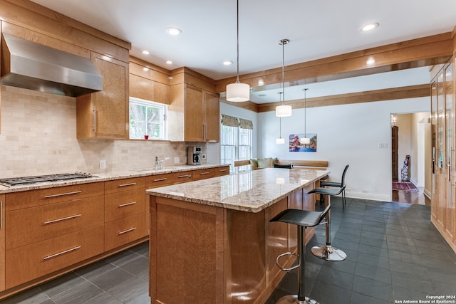 kitchen with hanging light fixtures, stainless steel gas cooktop, backsplash, wall chimney range hood, and a center island