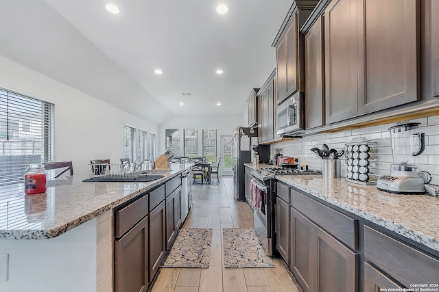 kitchen featuring vaulted ceiling, decorative backsplash, light stone countertops, appliances with stainless steel finishes, and a kitchen bar