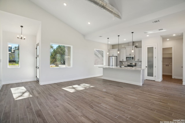 unfurnished living room featuring hardwood / wood-style floors, high vaulted ceiling, and an inviting chandelier