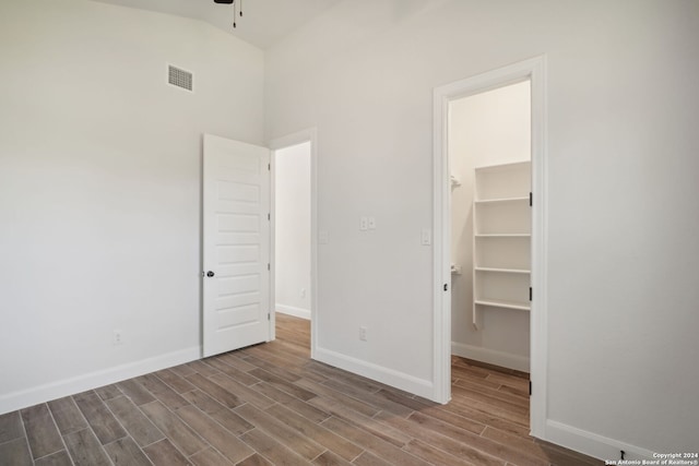 unfurnished bedroom with a spacious closet, a closet, high vaulted ceiling, and hardwood / wood-style flooring