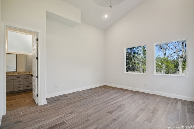 unfurnished bedroom with high vaulted ceiling, light hardwood / wood-style floors, and ensuite bath