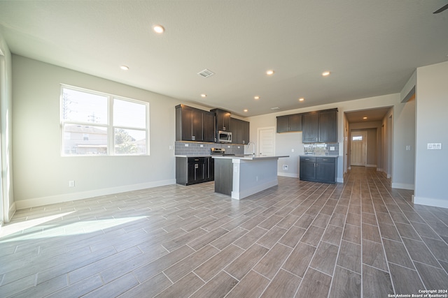 kitchen featuring a center island with sink, stainless steel appliances, dark brown cabinetry, and light hardwood / wood-style floors