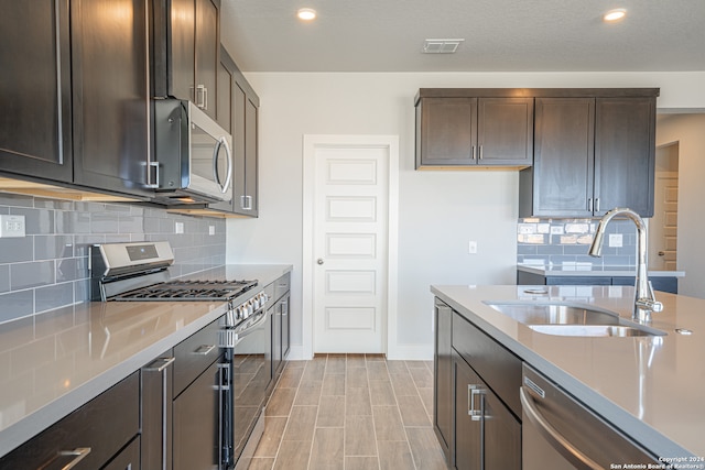 kitchen with dark brown cabinetry, decorative backsplash, stainless steel appliances, sink, and light hardwood / wood-style floors