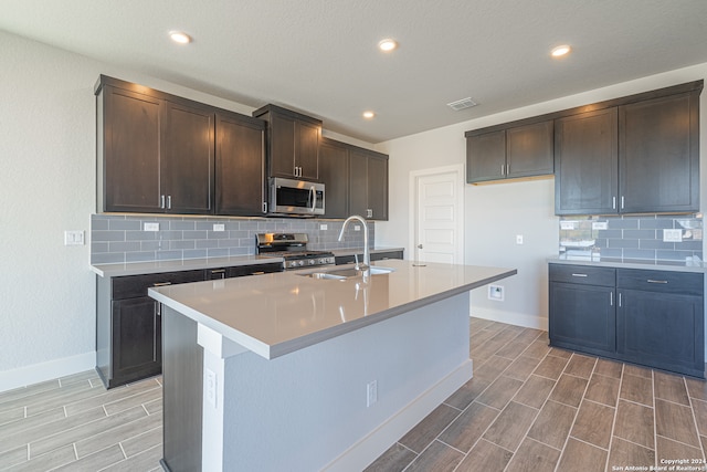 kitchen featuring dark brown cabinetry, sink, a center island with sink, light hardwood / wood-style flooring, and stainless steel appliances