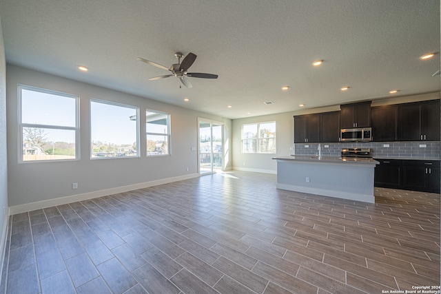 kitchen featuring light hardwood / wood-style flooring, a center island with sink, backsplash, appliances with stainless steel finishes, and a textured ceiling