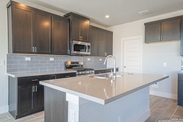 kitchen with a center island with sink, appliances with stainless steel finishes, sink, and dark brown cabinetry