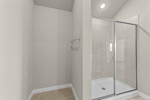 bathroom with tile patterned flooring, lofted ceiling, a shower with door, and a textured ceiling